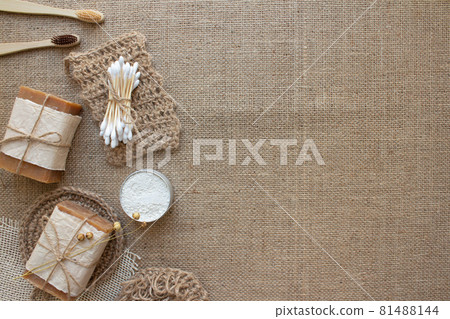 Top view on different natural bathroom tools, sustainable lifestyle, zero waste concept. Wooden toothbrushes, bamboo swabs, soap, toothpowder and jute washclothes on fabric background with copy space 81488144