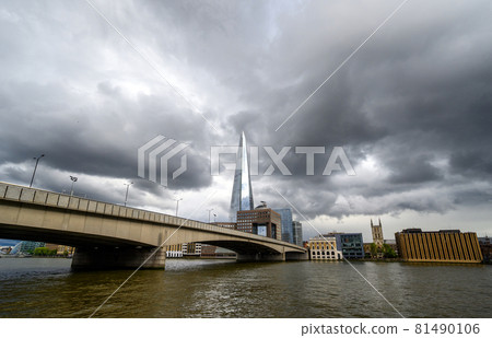 London, UK: View from the City of London looking south across the River Thames with London Bridge and the Shard building. Light reflecting on The Shard with dark storm clouds behind. 81490106