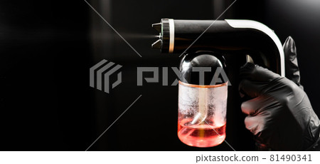 Close-up of instant tanning equipment in the hands of a master. Gun spraying paint for leather against black background Close-up of instant tanning equipment in the hands of a master. Gun spraying paint for leather against black background 81490341