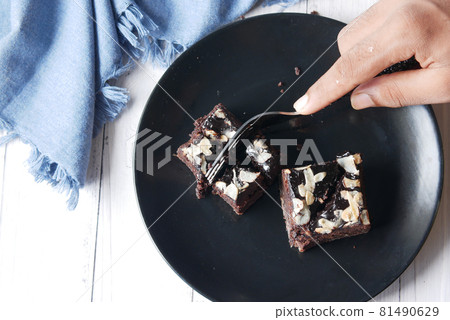 cutting slice of brownie with fork on plate on table  81490629