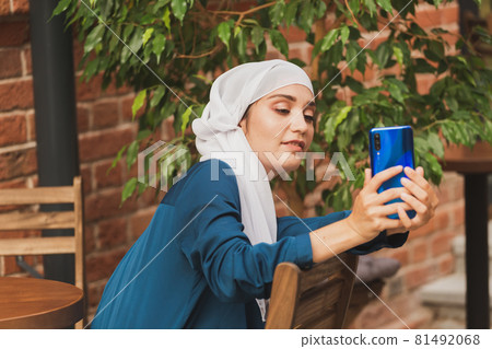 Muslim woman taking selfie. Happy beautiful girl with scarf take picture of her self using smartphone. Muslim woman taking selfie. Happy beautiful girl with scarf take picture of her self using smartphone. 81492068