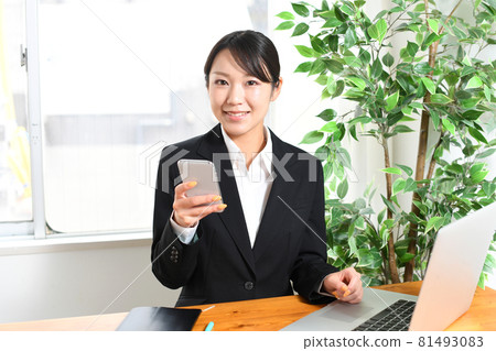 Image of a young black-haired woman in a suit looking at a smartphone / smartphone (mobile phone) 81493083