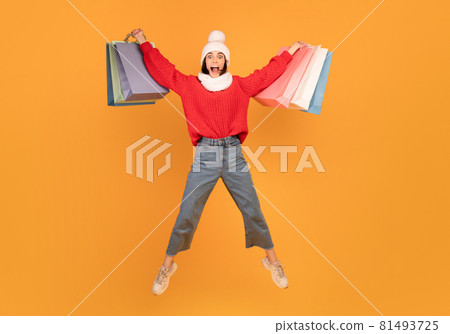 Big sales concept. Joyful shopaholic lady jumping with shopping bags, wearing knitted hat and winter jacket 81493725