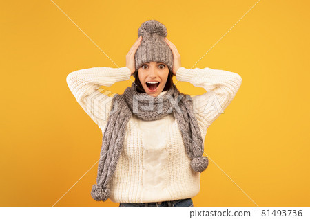 Wow, such a nice deal. Overjoyed lady in knitted hat and scarf looking at camera with open mouth, yellow background 81493736
