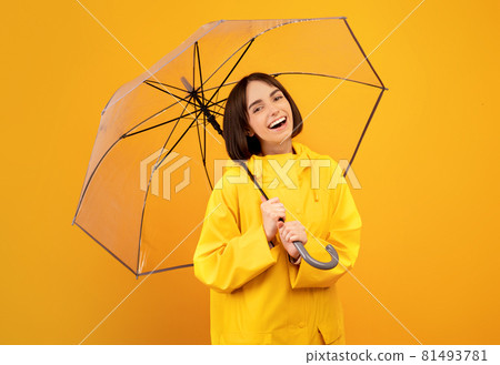 Autumn season concept. Portrait of happy lady standing under umbrella and smiling at camera over yellow background 81493781