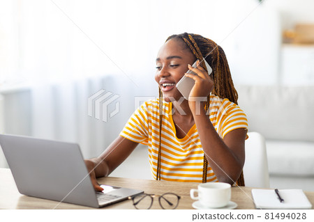 Positive black woman freelancer talking on phone and using laptop 81494028