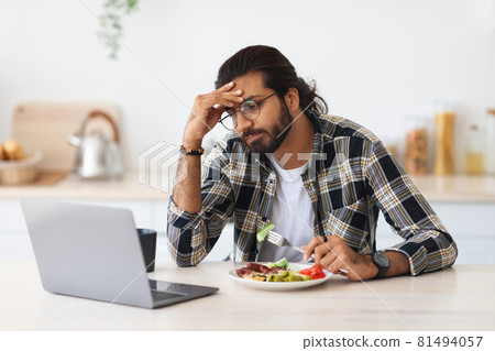 Exhausted middle-eastern man freelancer having snack while working from home Exhausted middle-eastern man freelancer having snack while working from home 81494057