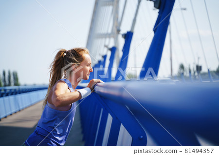 Mid adult woman runner stretching outdoors on bridge in city, healthy lifestyle concept. Mid adult woman runner stretching outdoors on bridge in city, healthy lifestyle concept. 81494357