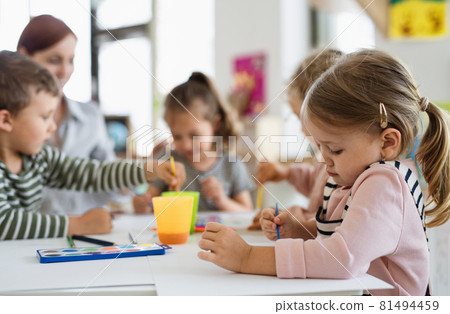 Group of small nursery school children with teacher indoors in classroom, painting. Group of small nursery school children with teacher indoors in classroom, painting. 81494459