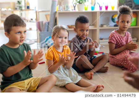 Group of small nursery school children sitting on floor indoors in classroom, clapping. Group of small nursery school children sitting on floor indoors in classroom, clapping. 81494479