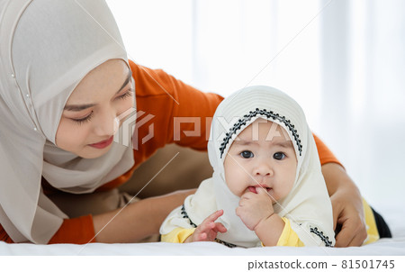 A cute and beautiful Asian Muslim in hijab dress playing with her daughter on bed A cute and beautiful Asian Muslim in hijab dress playing with her daughter on bed 81501745