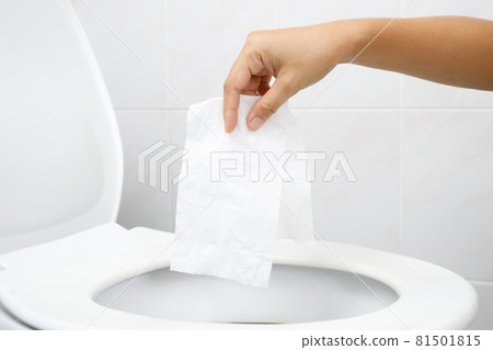 close up hand holding a tissue to be thrown into the toilet bowl. Can not drain water of toilet paper in cause the stool to clog up. WC 81501815