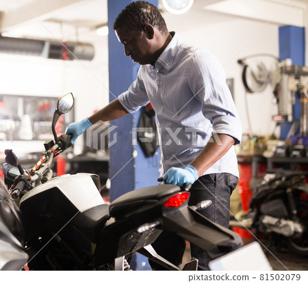 Afro american man working at restoring motorbike in motorcycle workshop 81502079