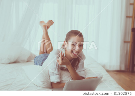 Happy woman shopping online and using laptop in bedroom 81502875