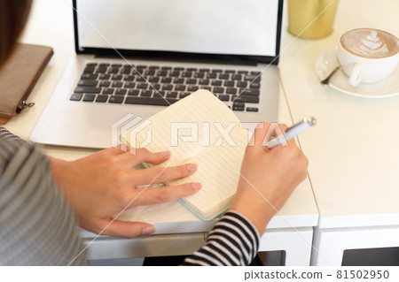Closeup, Female accountant taking notes on notebook with opened laptop on desk Closeup, Female accountant taking notes on notebook with opened laptop on desk 81502950