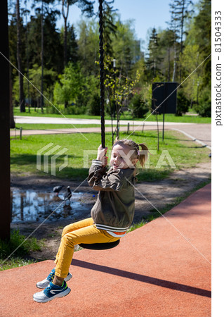 Caucasian little girl rides a bungee swing on the playground on a sunny day. Caucasian little girl rides a bungee swing on the playground on a sunny day. 81504333