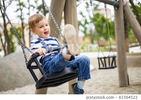 Smiling boy riding on swing at amusement forest park or childish playground having positive emotion 81504522