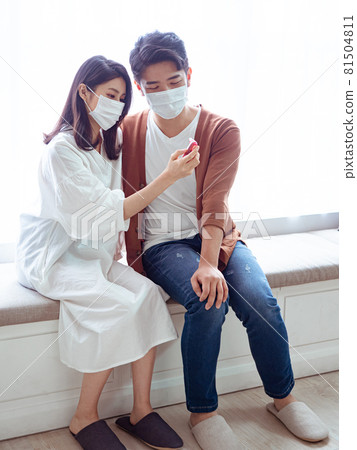 亞洲年輕女性和亞洲年輕男性在家戴外科口罩防止隔離感染新冠肺炎或流感 亞洲年輕女性和亞洲年輕男性在家戴外科口罩防止隔離感染新冠肺炎或流感 81504811