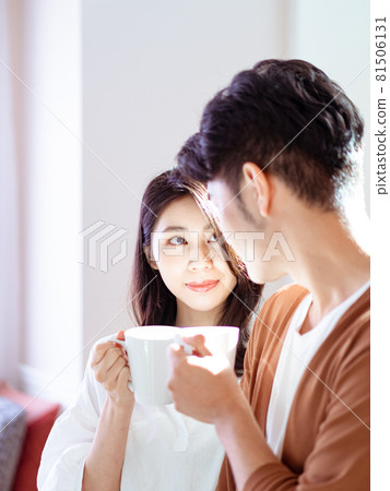 年輕的亞洲女人和男人在家裡，手裡個自拿著一杯咖啡。 81506131