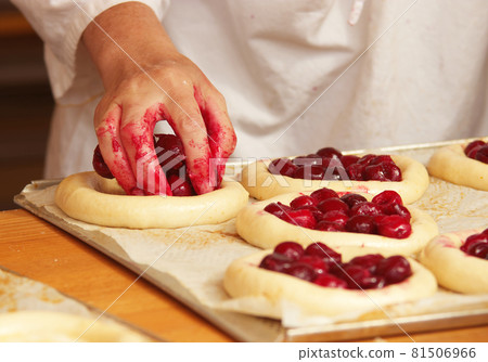 The woman in the picture is making filled fruit pies. Hands filling pie yeast dough with strawberries. Work in the bakery. 81506966