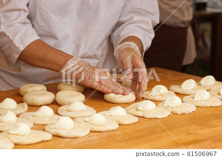 The woman in the picture is making stuffed pies. Hands in protective gloves wraps the curd filling into the yeast dough. Work in the bakery. 81506967