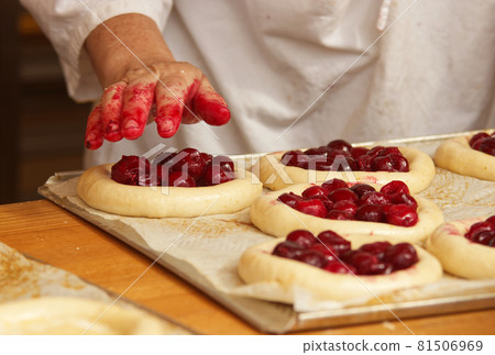 The woman in the picture is making filled fruit pies. Hands filling pie yeast dough with strawberries. Work in the bakery. 81506969