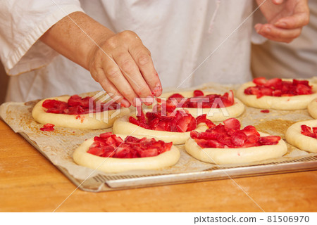 The woman in the picture is making filled fruit pies. Hands filling pie yeast dough with strawberries. Work in the bakery. 81506970