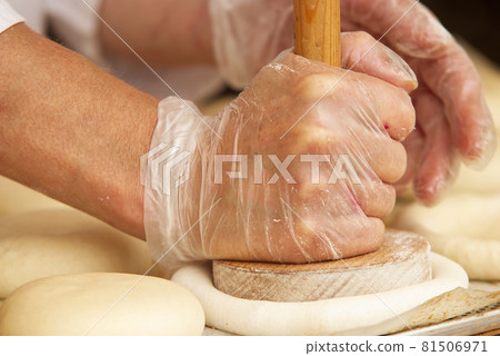 The woman in the picture is making stuffed pies. Hands in protective gloves holding the tool press dough to get the proper shape of pie. Work in the bakery. 81506971