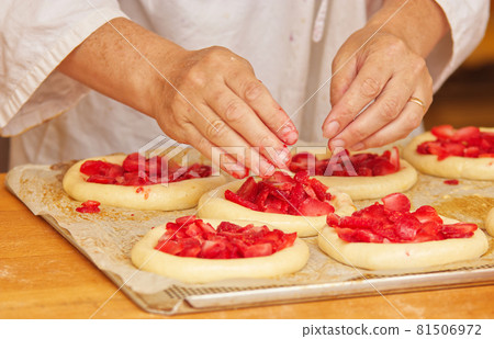 The woman in the picture is making filled fruit pies. Hands filling pie yeast dough with strawberries. Work in the bakery. 81506972