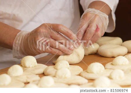 The woman in the picture is making stuffed pies. Hands in protective gloves wraps the curd filling into the yeast dough. Work in the bakery. 81506974