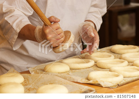 The woman in the picture is making stuffed pies. Hands in protective gloves holding the tool press dough to get the proper shape of pie. Work in the bakery. 81507148