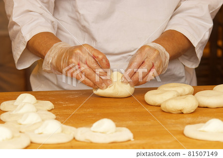 The woman in the picture is making stuffed pies. Hands in protective gloves wraps the curd filling into the yeast dough. Work in the bakery. 81507149