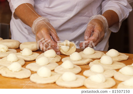 The woman in the picture is making stuffed pies. Hands in protective gloves wraps the curd filling into the yeast dough. Work in the bakery. 81507150