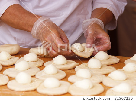 The woman in the picture is making stuffed pies. Hands in protective gloves wraps the curd filling into the yeast dough. Work in the bakery. 81507239