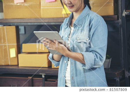 Asian woman startup small business at home office. Online seller entrepreneur young asian woman use tablet checking online order. Woman using tablet check stock goods supply delivery package shipping Asian woman startup small business at home office. Online seller entrepreneur young asian woman use tablet checking online order. Woman using tablet check stock goods supply delivery package shipping 81507809