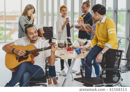 Asian worker playing the guitar over the Group Of Asian and Multiethnic Business people with casual suit talking and eatting with happy action when lunch time in the creative office workplace, life style and relax work concept 81508313