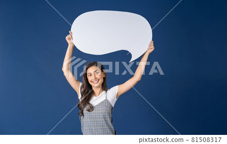 Happy young smiling Asian woman holding and pointing to copy space empty message bubbles on blue color background, thinking and specking via balloon blank paper, Private opinion Concept 81508317