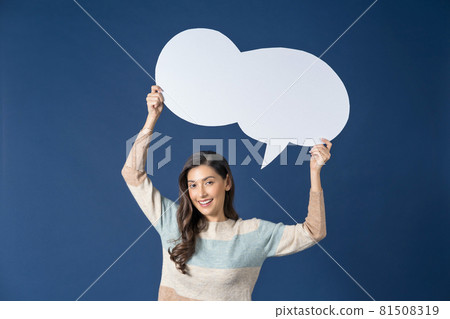 Happy young smiling Asian woman holding and pointing to copy space empty message bubbles on blue color background, thinking and specking via balloon blank paper, Private opinion Concept 81508319