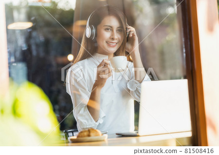 Portrait Young Asian woman holding a cup of coffee and using technology laptop in a coffee shop for working and listening music, freelancer and entrepreneur working by connecting to internet. Portrait Young Asian woman holding a cup of coffee and using technology laptop in a coffee shop for working and listening music, freelancer and entrepreneur working by connecting to internet. 81508416