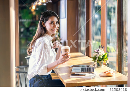 Portrait Young Asian woman holding and drinking a cup of coffee and working with technology laptop at a coffee shop. freelancer and entrepreneur working by connecting to internet via computer Portrait Young Asian woman holding and drinking a cup of coffee and working with technology laptop at a coffee shop. freelancer and entrepreneur working by connecting to internet via computer 81508418