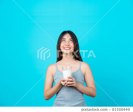 Attractive Asian young woman holding milk on isolated blue color background, weight loss and avoid junk food for dieting and Healthy Attractive Asian young woman holding milk on isolated blue color background, weight loss and avoid junk food for dieting and Healthy 81508449