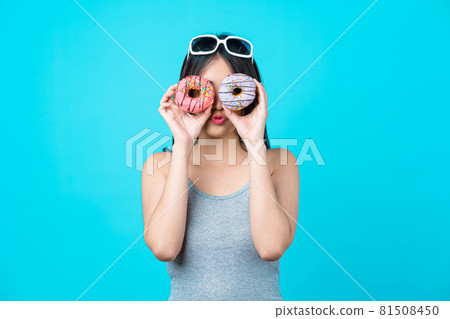Attractive Asian young woman smiling and playing with sweet donuts in her face on isolated blue color background, weight loss and avoid junk food for dieting and Healthy concept, copy space and studio Attractive Asian young woman smiling and playing with sweet donuts in her face on isolated blue color background, weight loss and avoid junk food for dieting and Healthy concept, copy space and studio 81508450