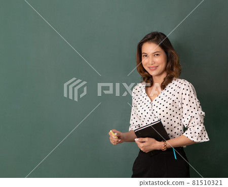 Beautiful Asian woman holding book and chalk standing in front of black board with copy space 81510321