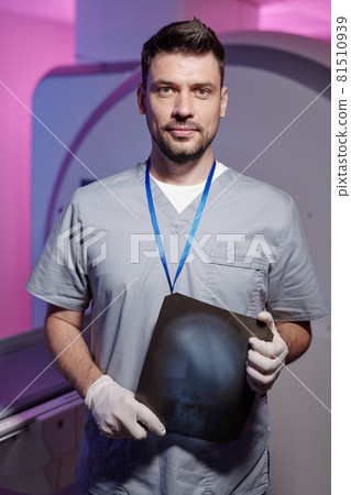 Confident radiologist in gloves and uniform standing against medical equipment 81510939