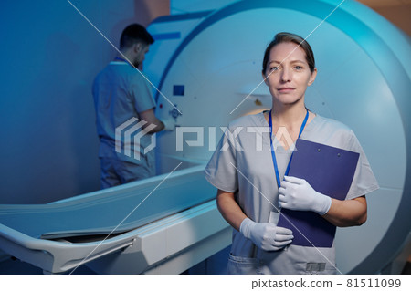Young nurse in uniform and gloves standing in front of medical machine Young nurse in uniform and gloves standing in front of medical machine 81511099