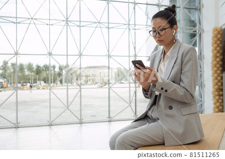 Young serious businesswoman with earphones watching video in smartphone Young serious businesswoman with earphones watching video in smartphone 81511265