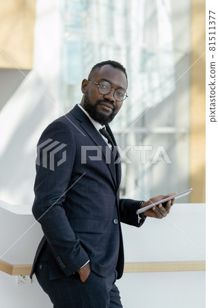 Young bearded businessman in eyeglasses and formalwear holding digital tablet 81511377