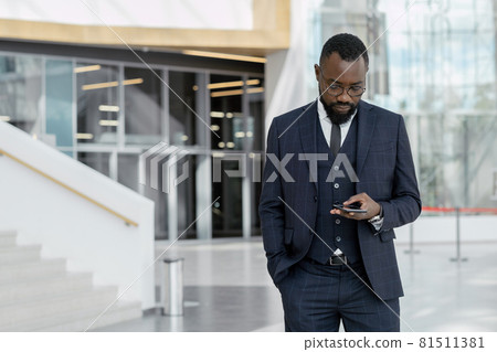 Young African-American broker in suit texting in smartphone 81511381