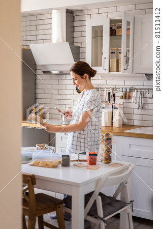 Happy female housewife smiling posing and takes pictures of the barcode at modern Nordic style kitchen food storage organization 81511412