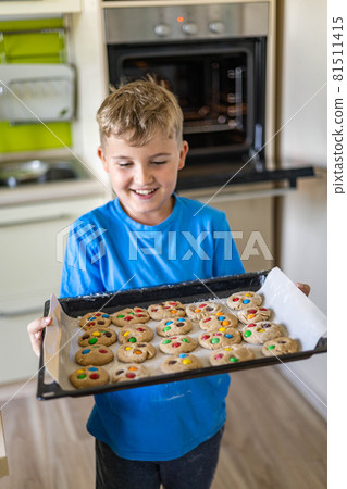 Portrait of happy baby boy posing with baking sheet full dessert with multicolored round chocolates m&m Portrait of happy baby boy posing with baking sheet full dessert with multicolored round chocolates m&m 81511415